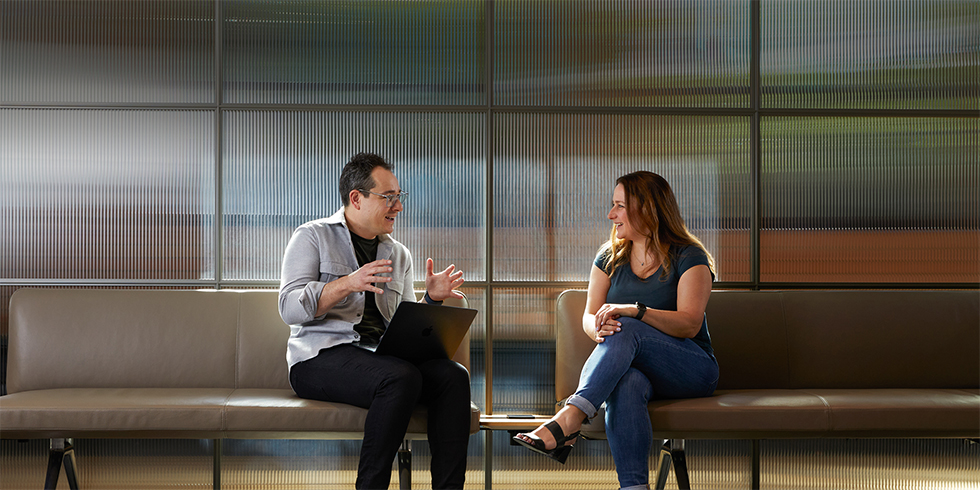 Dos colegas conversan sentados en las bancas en una zona común.