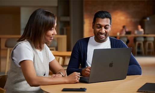 共通エリアのテーブルに置いたMacBookの前に座り、同僚と一緒に作業しているアマー。