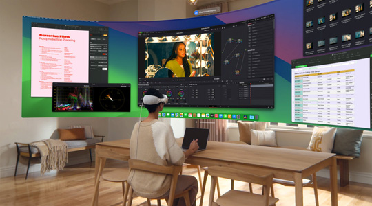 有人戴著 Apple Vision Pro 坐在桌前，桌上有打開狀態的 13 吋 MacBook Pro，螢幕內容以超寬闊曲面顯示器方式投影在房間內。
