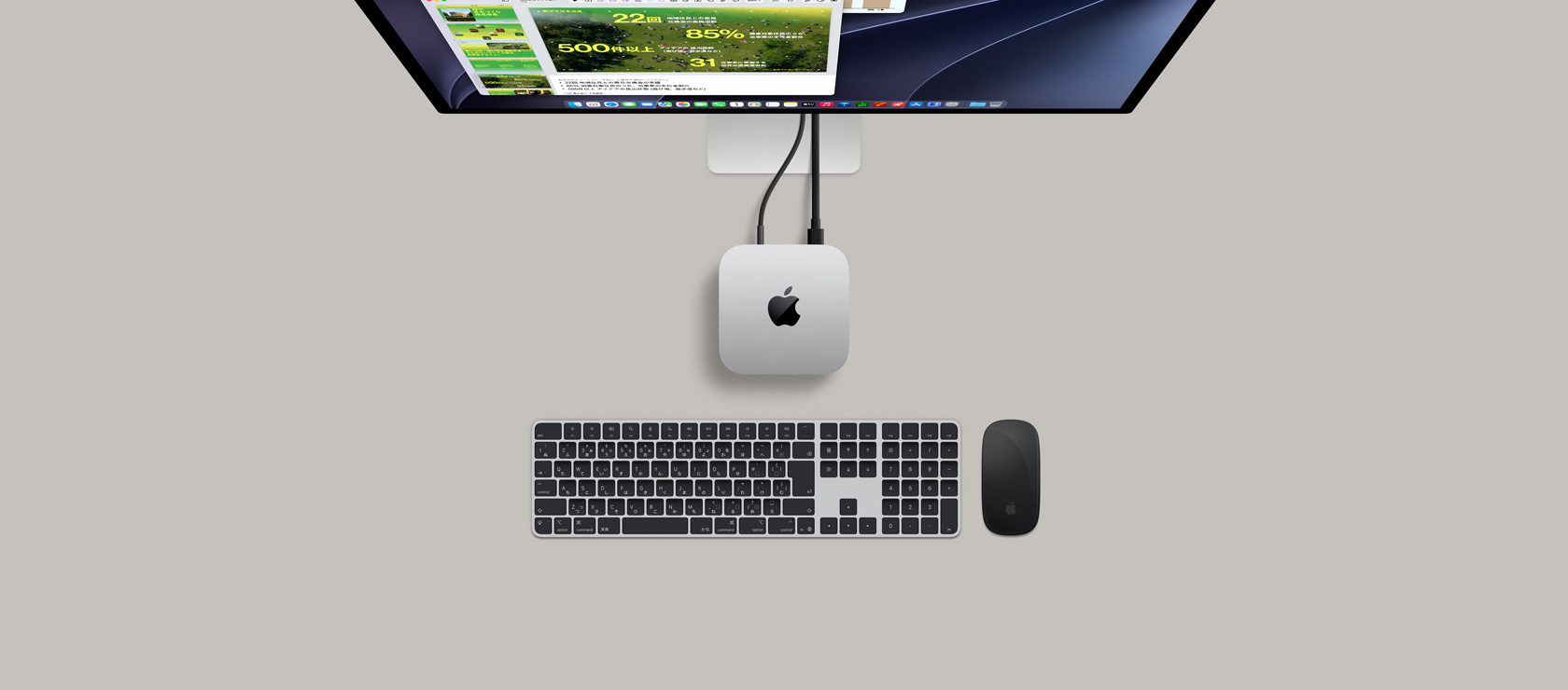 Mac miniを上から見た図。シルバーのアルミニウム、丸みを帯びた四隅、中央に光沢のあるブラックのAppleのロゴ。コードで接続されている。上部にStudio Displayの一部分が見えており、画面にカレンダーアプリ、Keynoteのプレゼンテーション、棒グラフが表示されている。Mac miniの下にテンキーが付いたMagic KeyboardとMagic Mouseが見えている