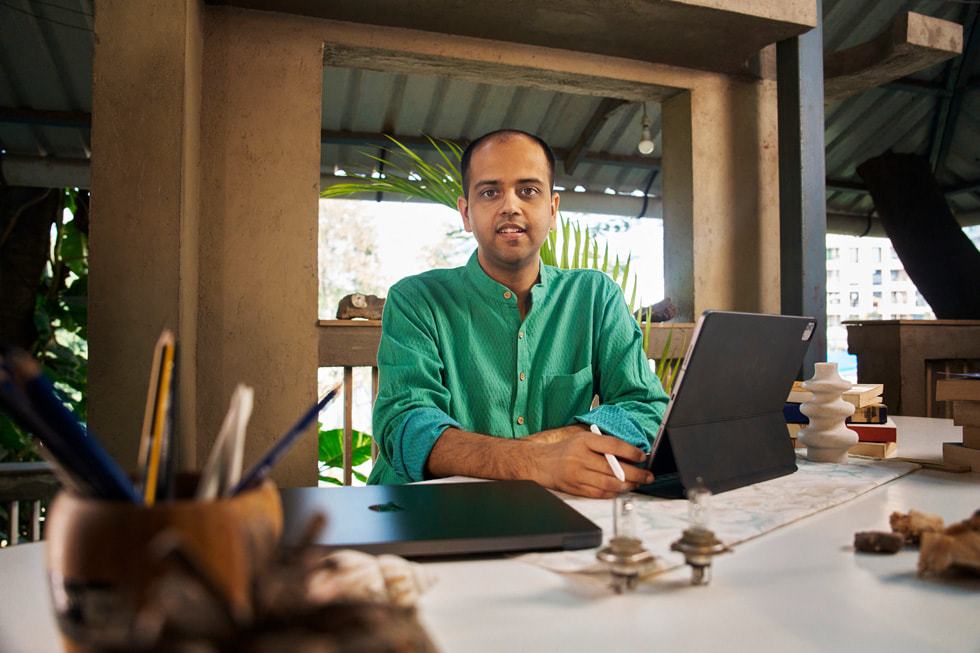 Dhruv Jani holds Apple Pencil, with iPad Pro and MacBook Pro on his desk.