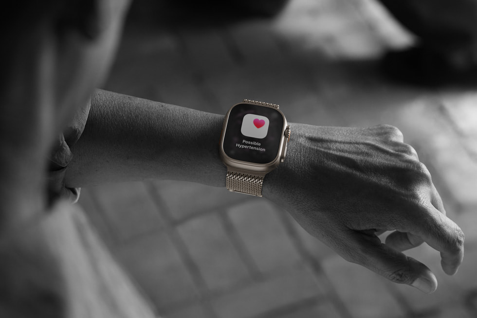 A black-and-white photo of a person checking their Apple Watch Ultra 3 and seeing the hypertension notifications screen with a red heart.