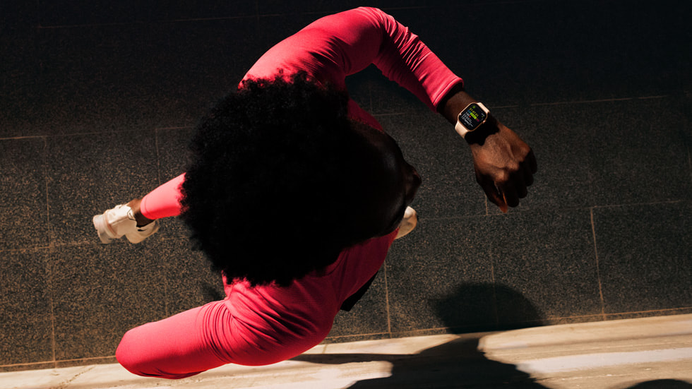 Eine Person rennt eine dunkle Straße entlang und schaut auf ihre Apple Watch, auf der Workout Buddy angezeigt wird.