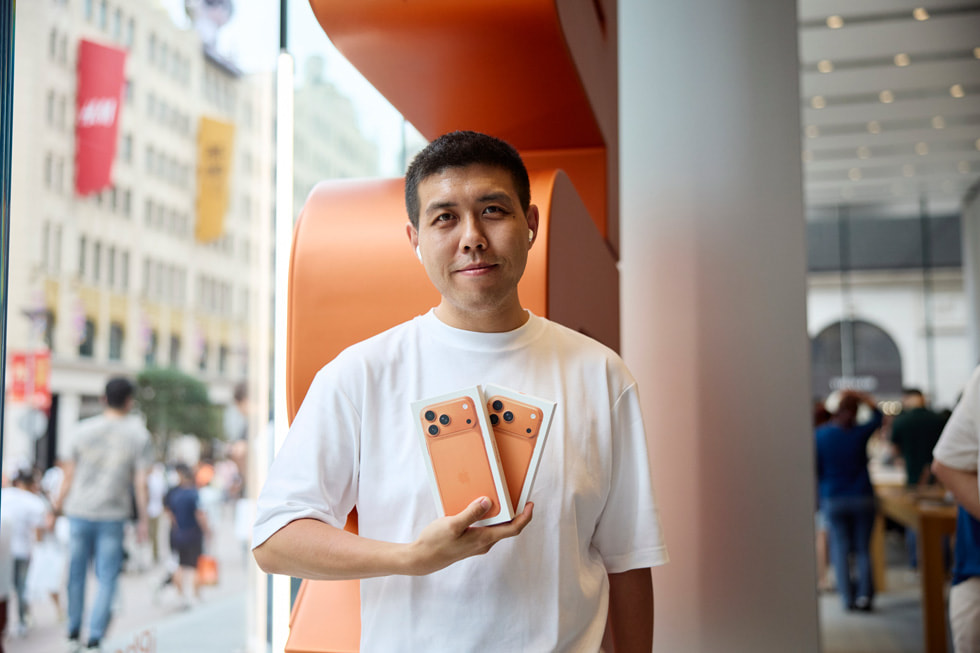 A customer wearing AirPods holds up two iPhone 17 Pro devices at Apple Nanjing East in Shanghai.