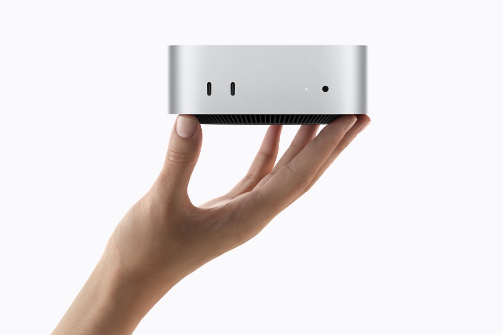 En hånd holder en sølvfarvet Mac mini, der viser portene på forsiden.