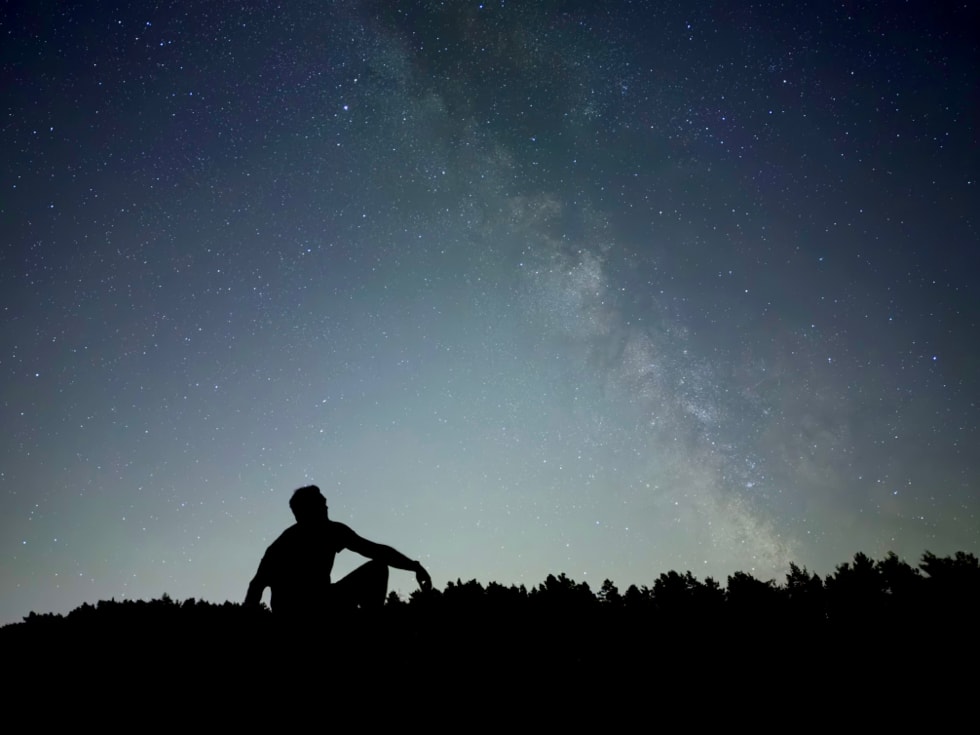 Foto tomada con un iPhone 18 Pro usando el modo Noche que muestra la silueta de una persona bajo un cielo estrellado.