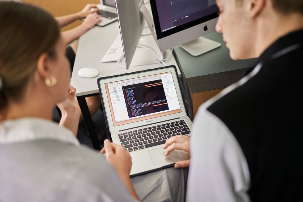 A Siena Catholic College student and instructor review code on MacBook Air.
