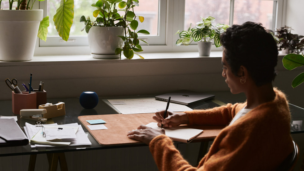A man working on his desk with a blue HomePod mini by his side.