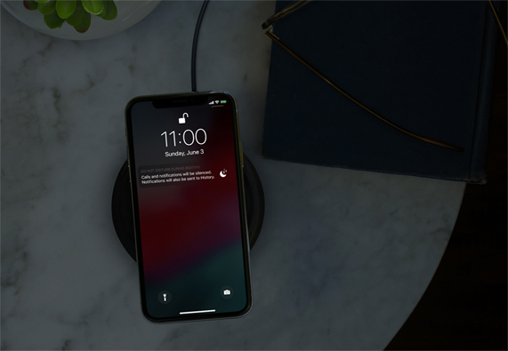 iPhone in a dark room on a wireless charger showing Do Not Disturb.