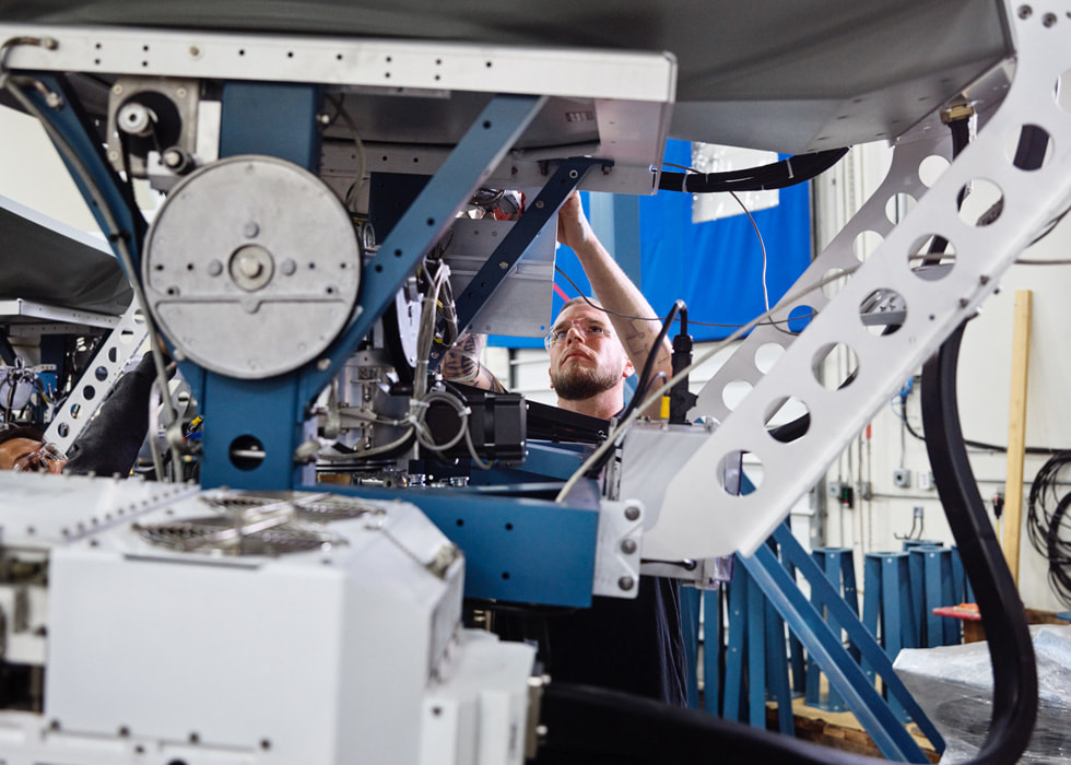 A worker examines a satellite in an indoor setting.