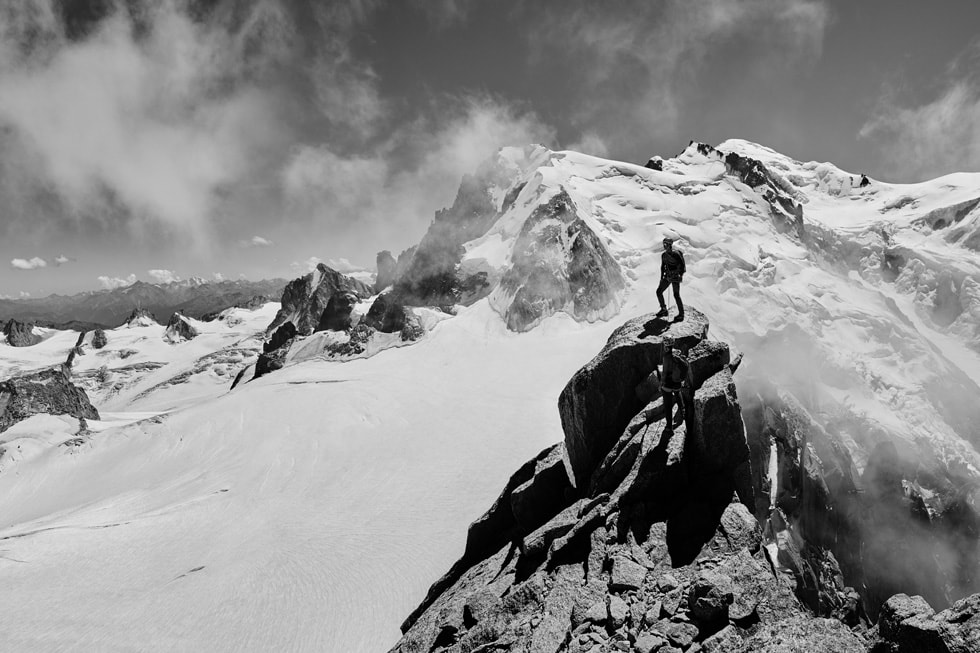 Eine Person mit Apple Watch Ultra auf einem Berggipfel, umgeben von schneebedeckten Bergen. 