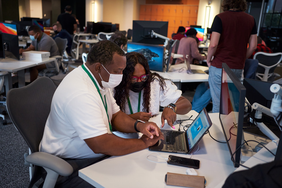 A mentor teaching a peer on a MacBook inside the Detroit Apple Developer Academy.