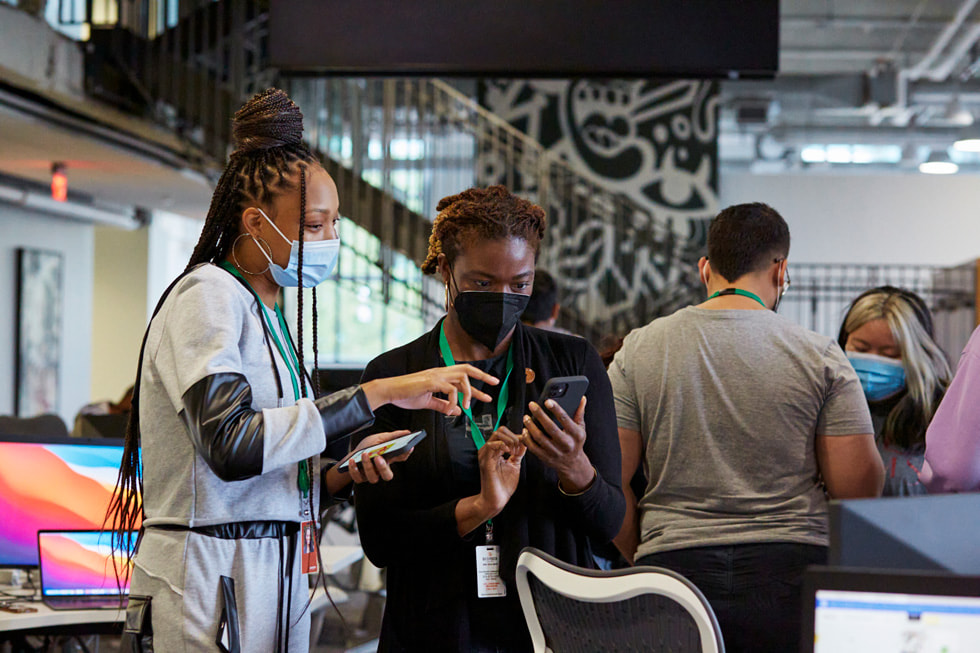 Two students learning the fundamentals of coding on their iPhone devices inside the Detroit Apple Developer Academy.