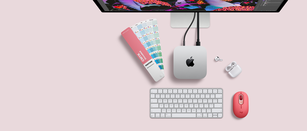 Mac mini, partea de sus, aluminiu argintiu, colțuri rotunjite, logo Apple negru lucios centrat, conectat prin cablu, monitorul Studio Display parțial vizibil de sus, căști AirPod 4, deschise, mostre de culoare Pantone, tastatură numerică și mouse