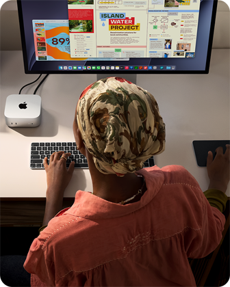 Niekto píše pri stole, na ktorom je Mac mini s pripojeným displejom Studio Display, klávesnica Magic Keyboard, trackpad Magic Trackpad a rôzne predmety