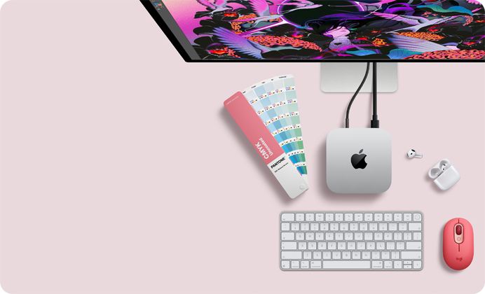 Mac mini, вид зверху, алюмінієвий корпус сріблястого кольору, заокруглені кути, глянцевий чорний логотип Apple по центру, підʼєднання за допомогою кабелю, Studio Display частково видно зверху, AirPods 4, відкриті, зразки кольорів Pantone, цифрова клавіатура та миша