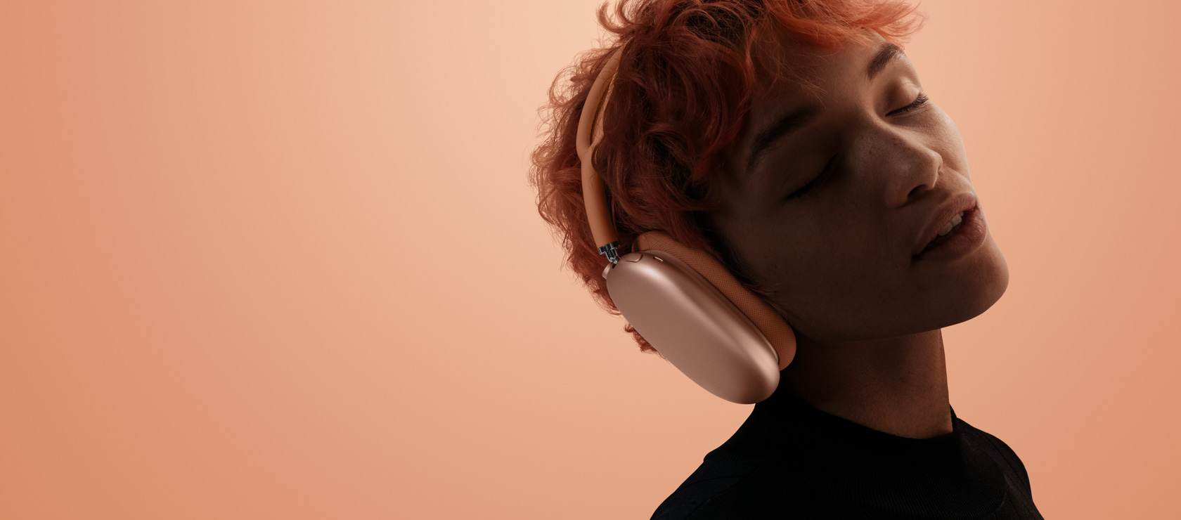 A person with head tilted and eyes closed wearing AirPods Max 2, orange color, over orange-pink background