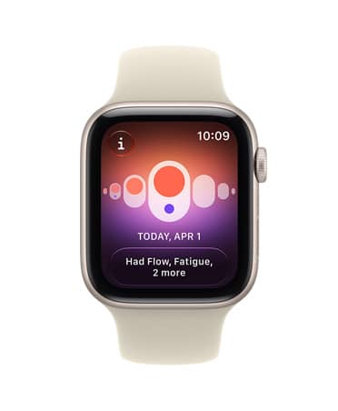 Apple Watch SE 3 z aluminiową kopertą w kolorze księżycowej poświaty i paskiem sportowym w kolorze piasku (jasnobeżowym). Na ekranie widać funkcje zdrowotne (śledzenie cyklu). Na prawym boku urządzenia pokrętło Digital Crown.