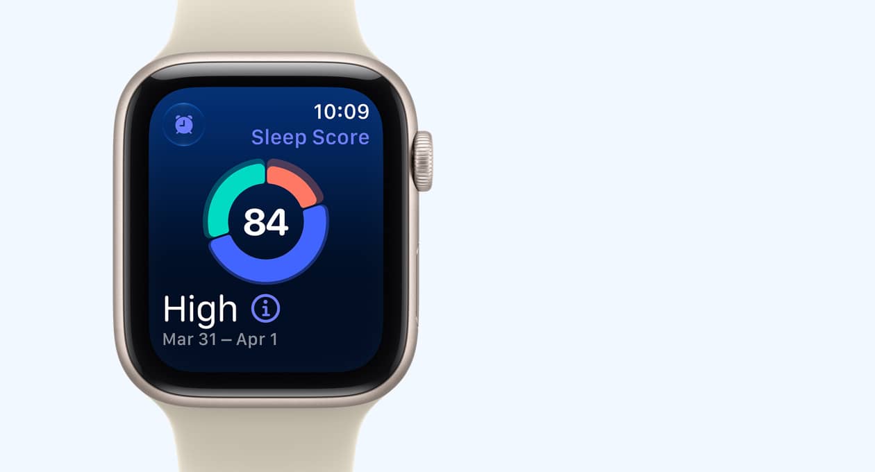 Apple Watch SE 3 z aluminiową kopertą w kolorze księżycowej poświaty i paskiem sportowym w kolorze piasku (jasnobeżowy) wyświetla na ekranie wykres kołowy z wynikiem snu. Na prawym boku urządzenia pokrętło Digital Crown