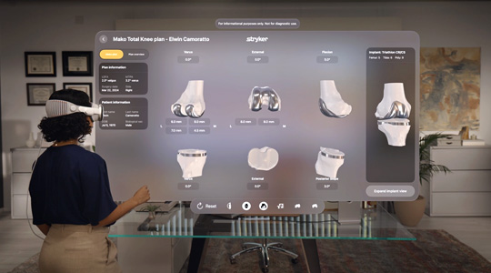 A surgeon wearing Apple Vision Pro interacts with a 3D projection of knee bones and joints, with metallic pieces attached to them