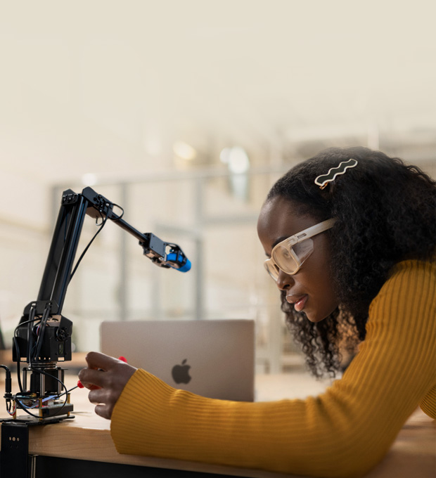 Image of a woman wearing lab glasses working on a robotic arm in a laboratory setting.