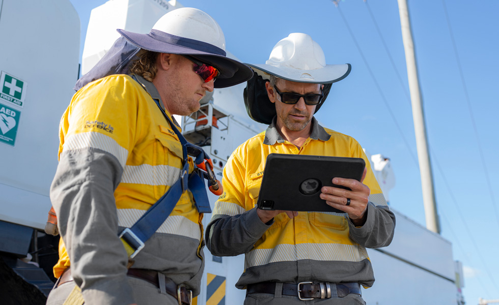 Two field workers collaborate on an iPad while standing beside a utility truck