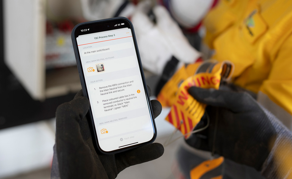Une main tient un iPhone qui affiche des instructions permettant de réaliser un test sur un panneau de contrôle, avec les mots « 13C Process Step 3 » à l’écran
