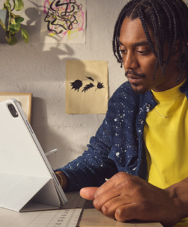Bir ofis ortamında oturan ve gümüş renkli 12.9 inç iPad Pro kullanan bir adam