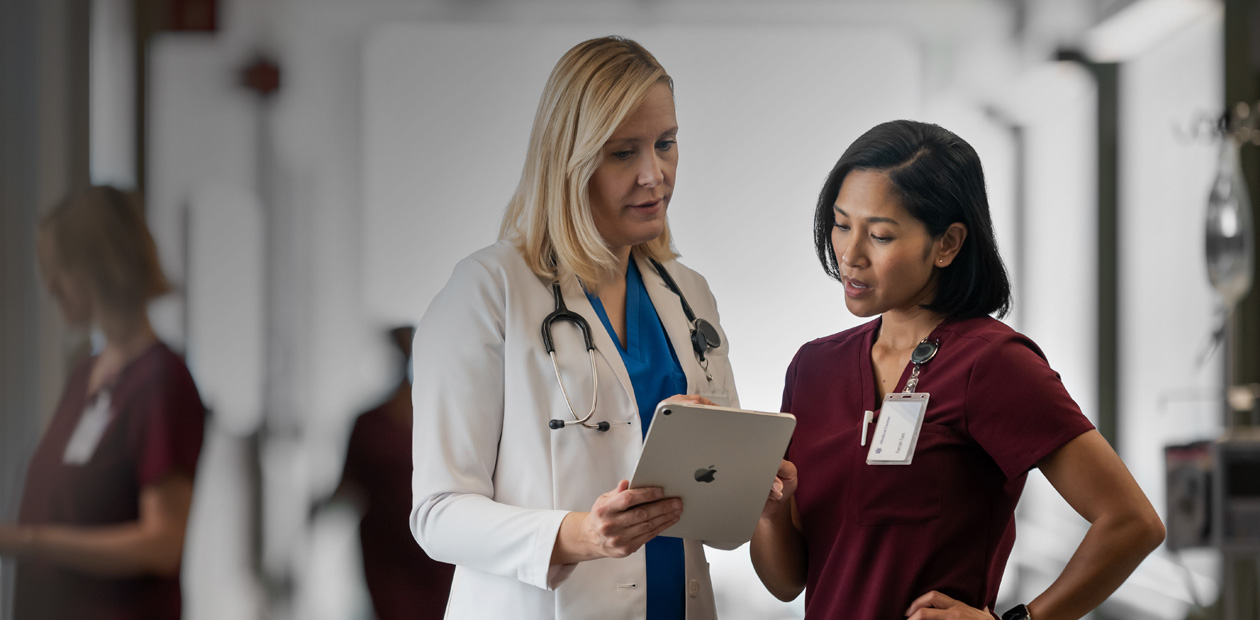 Eine Ärztin und eine Pflegerin sehen gemeinsam auf ein iPad in einem Krankenhausflur.