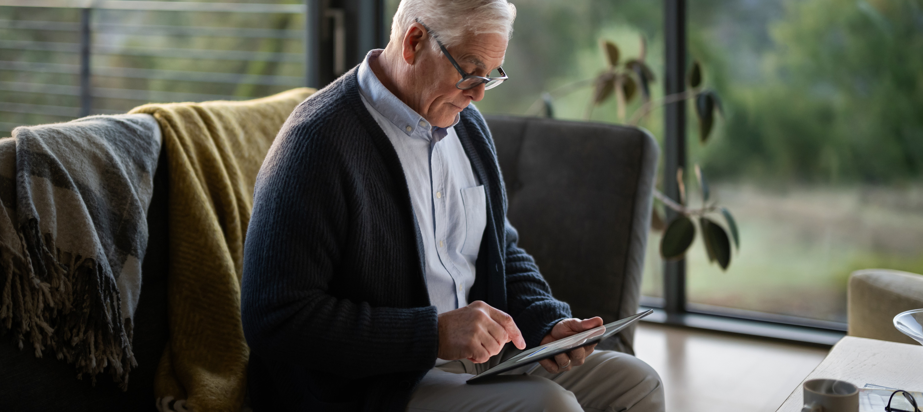 An elderly man sitting on a couch looking at an iPad.
