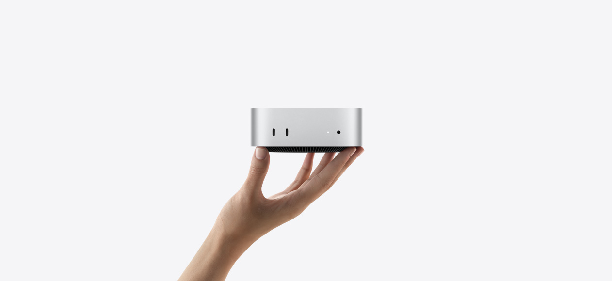 Вид спереду на Mac mini, який балансує на кінчиках пальців витягнутої вгору руки, на передній панелі розміщено два&nbsp;порти Thunderbolt, індикатор стану та порт для навушників, чорна звужена основа знизу, пласка верхня панель, заокруглені по боках, прямі краї, сріблястий колір