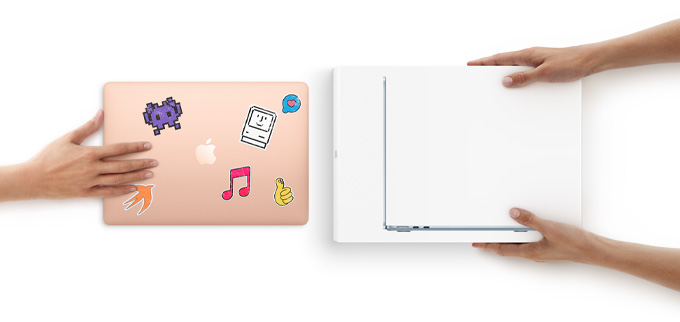 A hand slides a MacBook with stickers on the cover toward two hands holding a new MacBook in the box