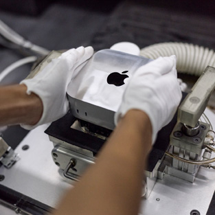 Montaj sırasında bir Mac mini’yi üretim makinesine yerleştiren eldivenli eller