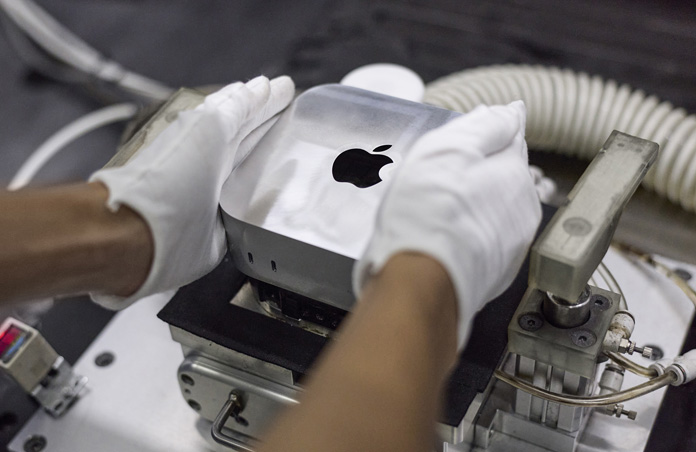 Montaj sırasında bir Mac mini’yi üretim makinesine yerleştiren eldivenli eller
