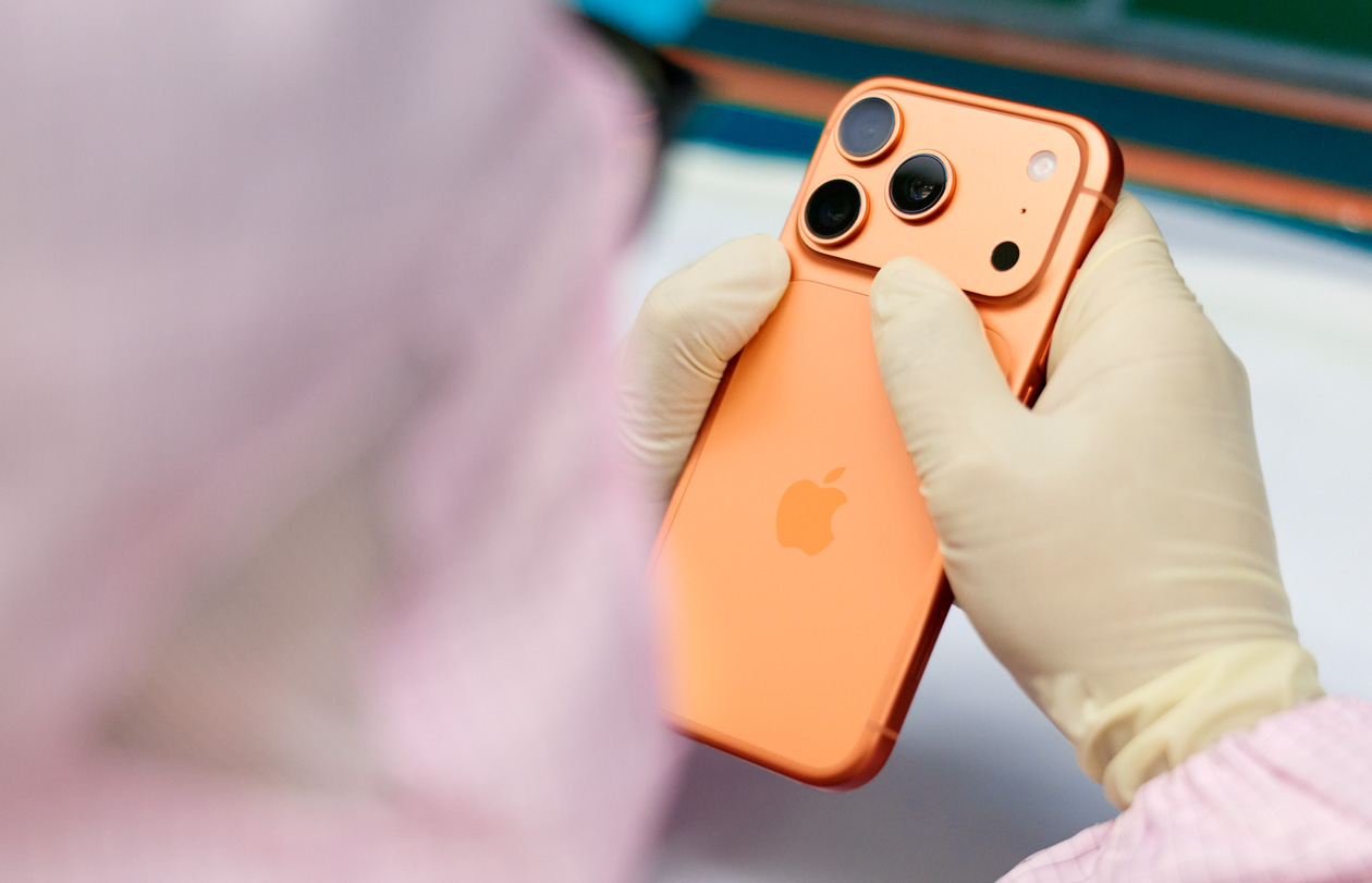 Tam korumalı iş tulumu giymiş bir çalışan, çalışma istasyonunda bir iPhone’u inceliyor