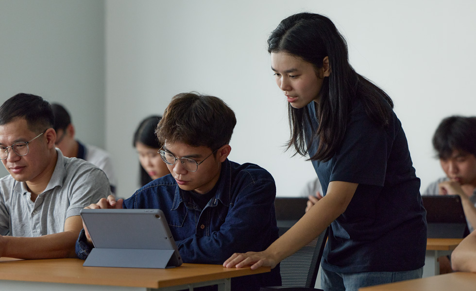 Sınıf ortamında iki kişi bir Apple tablette birlikte çalışıyor