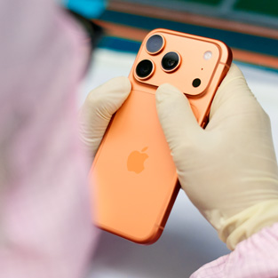 Tam korumalı iş tulumu giymiş bir çalışan, çalışma istasyonunda bir iPhone’u inceliyor