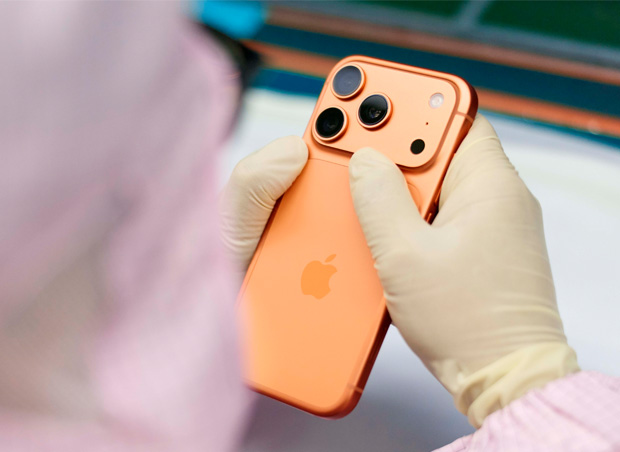 Tam korumalı iş tulumu giymiş bir çalışan, çalışma istasyonunda bir iPhone’u inceliyor
